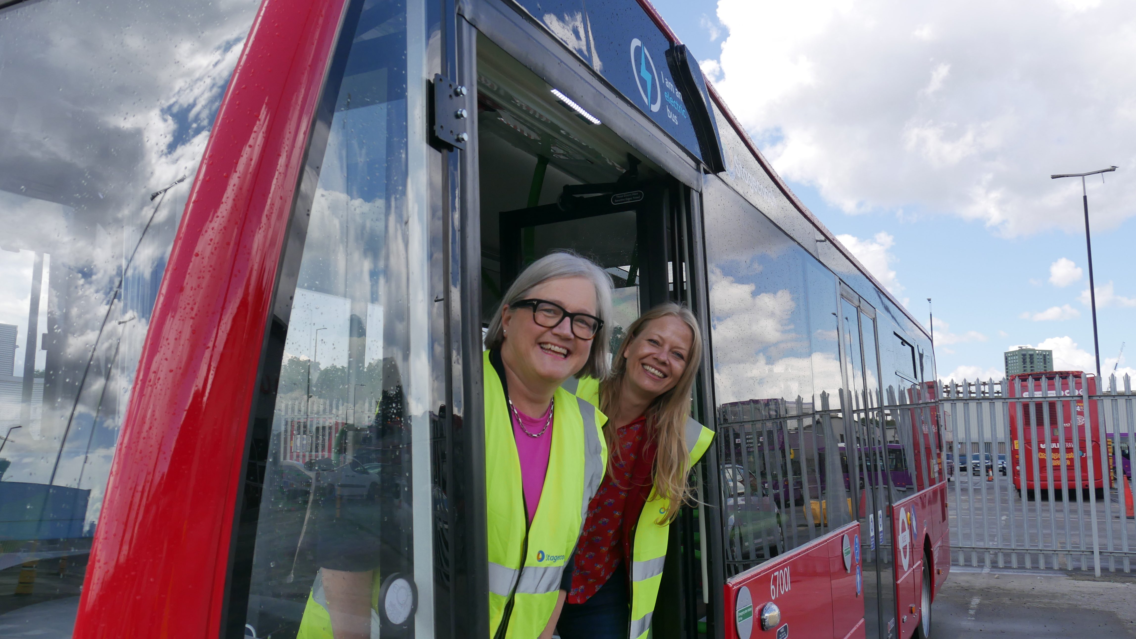 Caroline Russell AM and former Green Siân Berry AM stick their heads out of a parked London bus with reflective vests. 