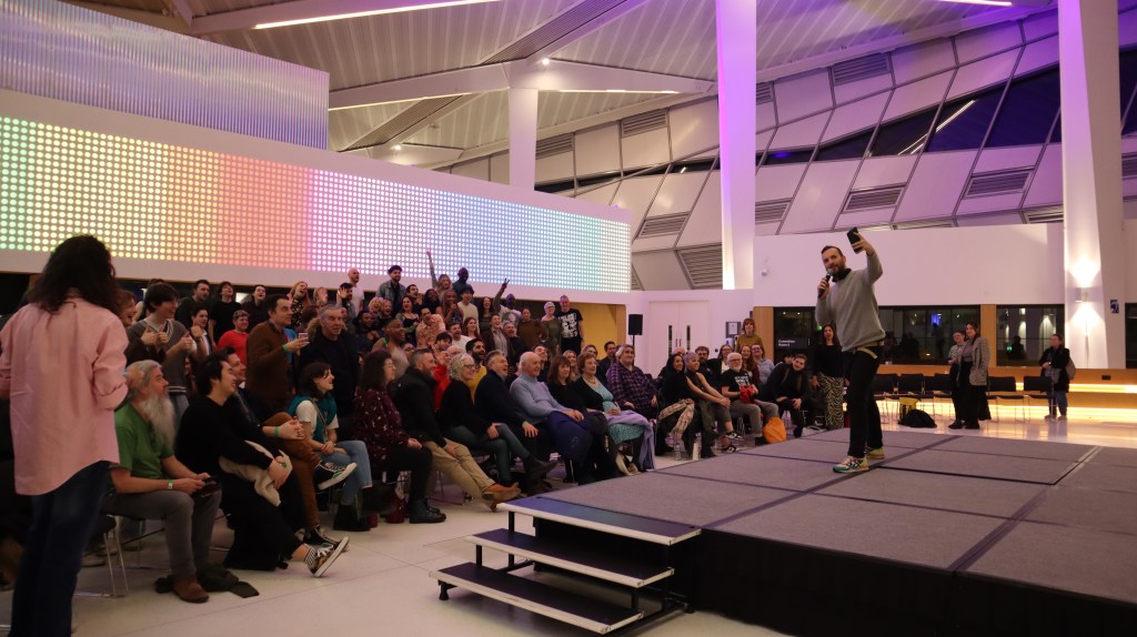 Zack Polanski stands on a stage taking a selfie with the audience after London's first ever theatrical production in the new City Hall. 