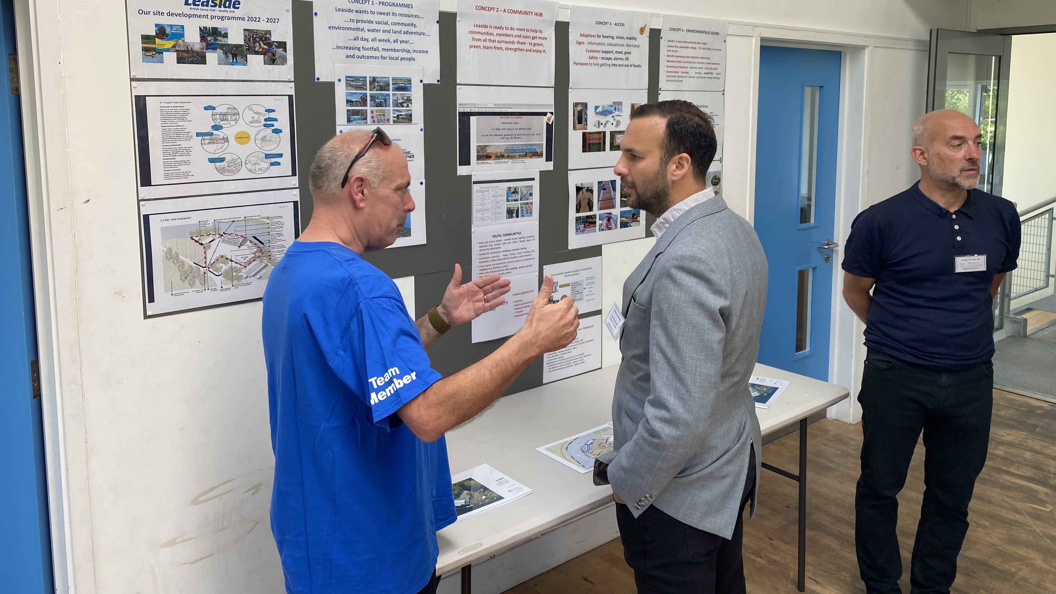 Zack Polanski speaks to an environmental activist regarding London's ecology. There are poster boards behind them as they speak. 