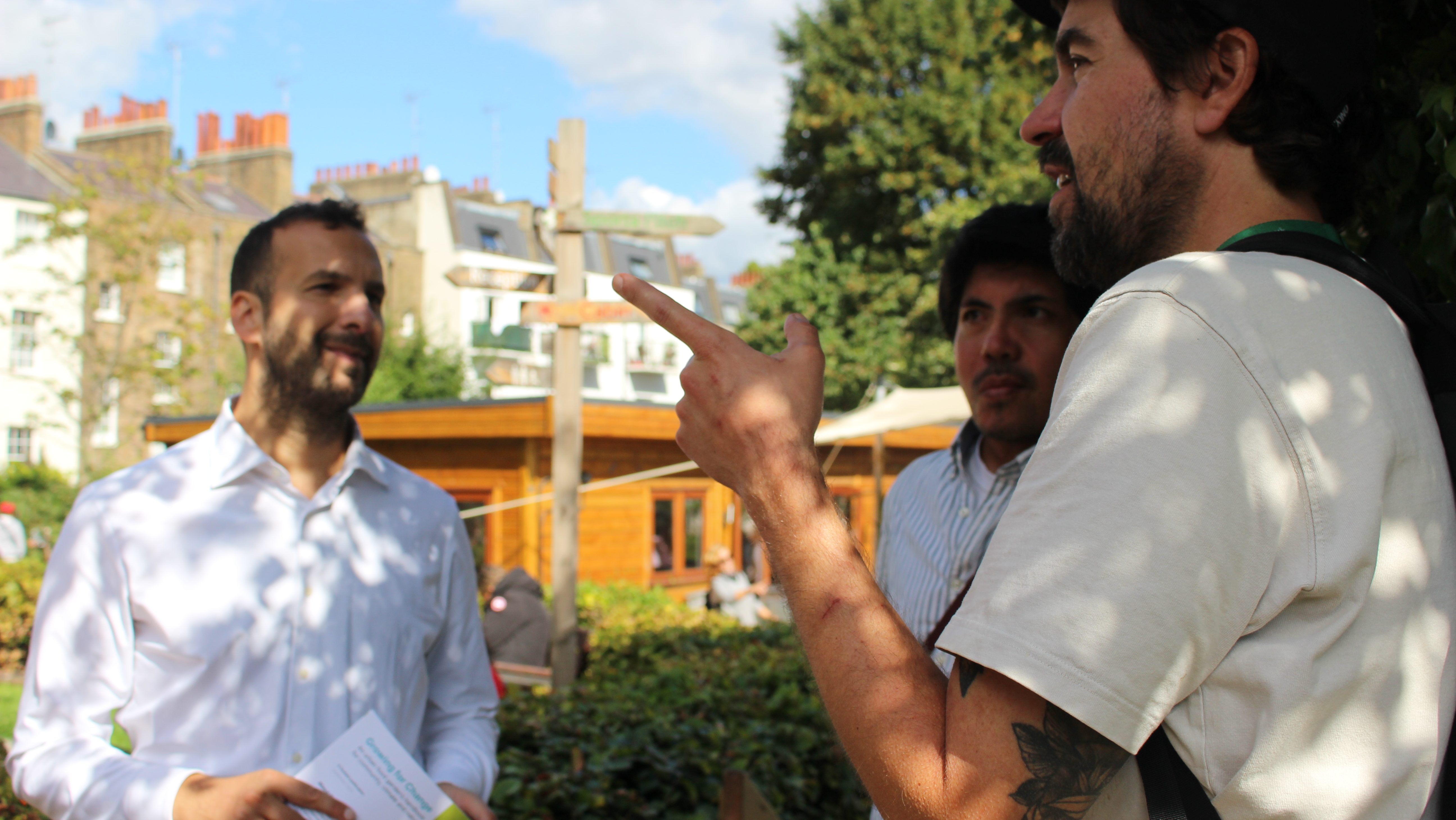 Zack Polanski speaks to two campaigners outdoors behind a residential block of London. 