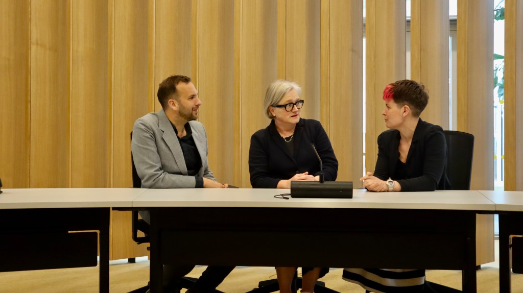 Zack Polanski AM, Zoë Garbett AM and Caroline Russell AM sit in City Hall's Chamber, facing each other in discussion. 