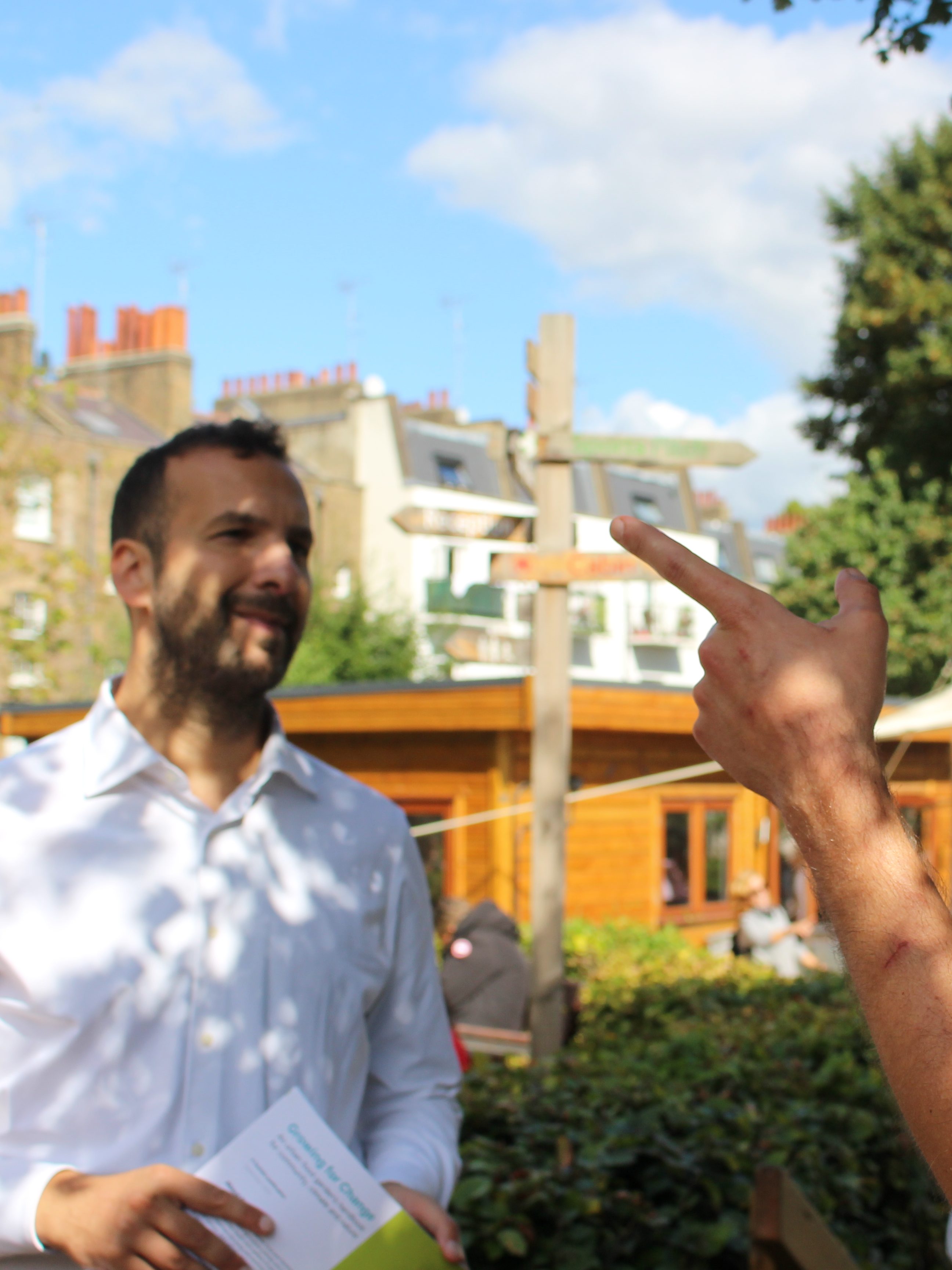 Zack Polanski speaks to two campaigners outdoors behind a residential block of London. 