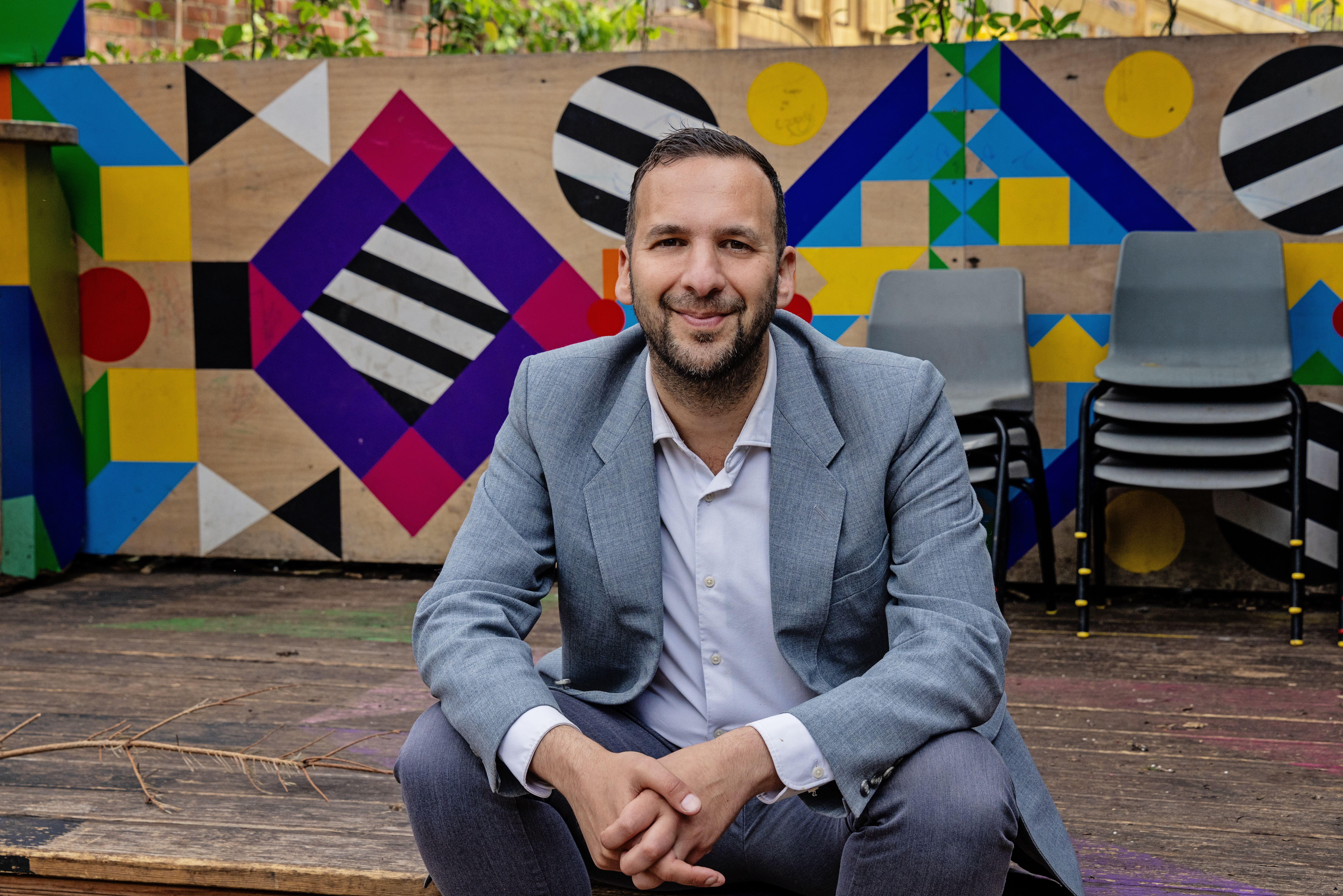Zack Polanski smiles into the camera in front of a local community theatre set.