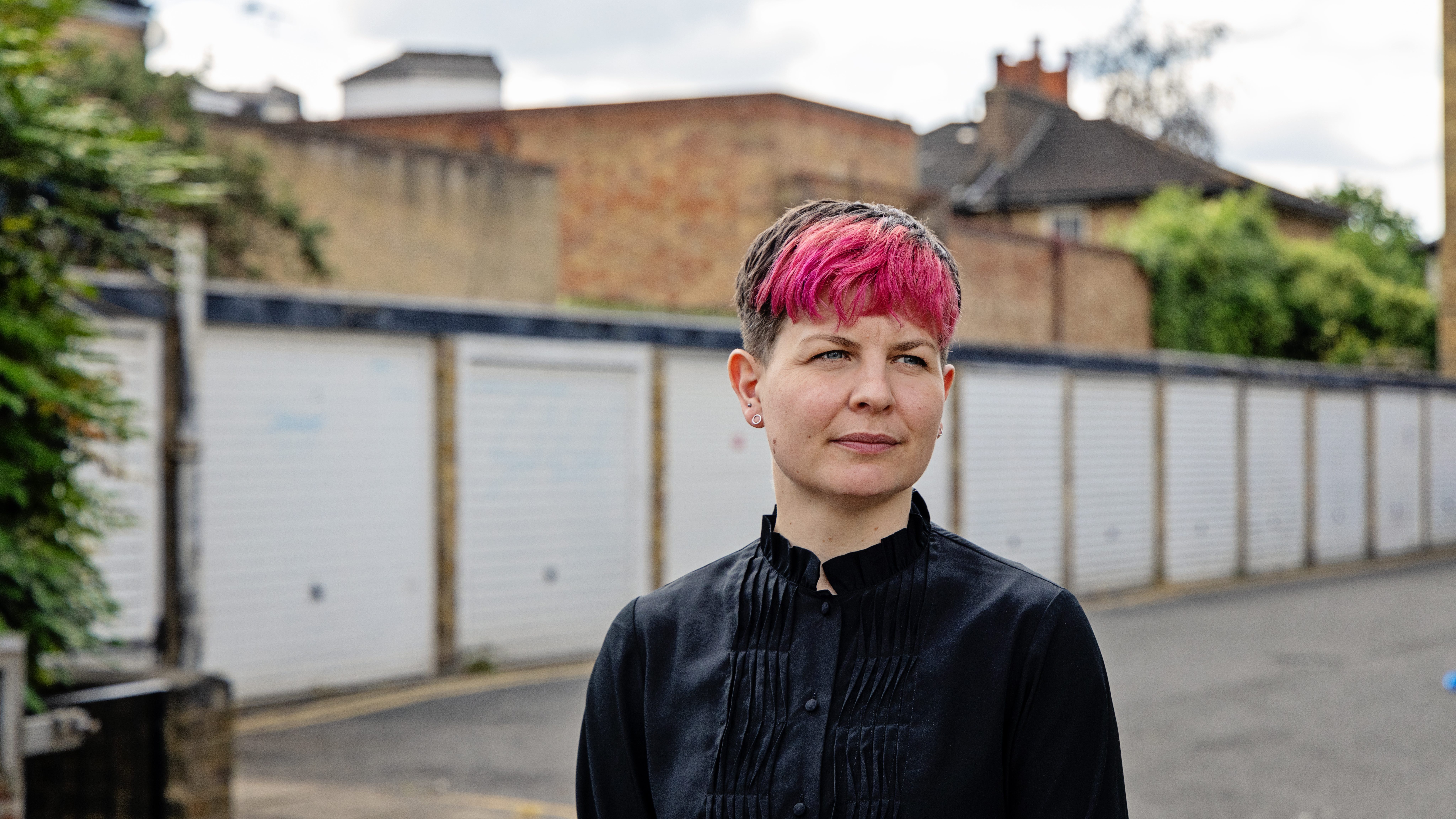 Headshot of Zoë Garbett AM looking into the distance while posing in front of garages. 