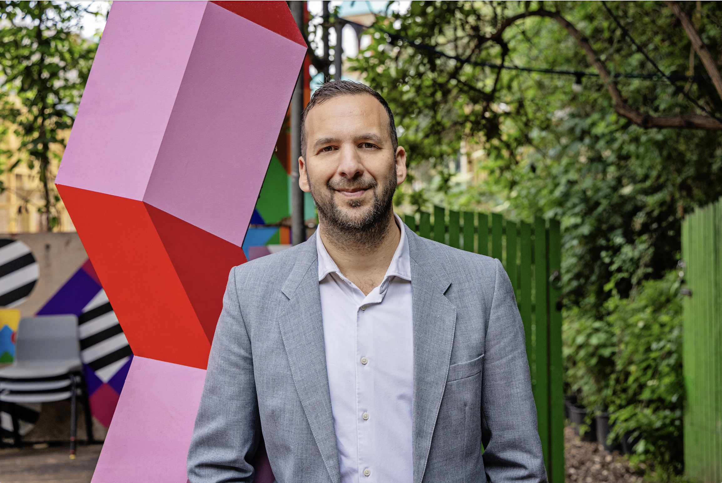 Zack Polanski smiles into the camera in front of a local community theatre set.